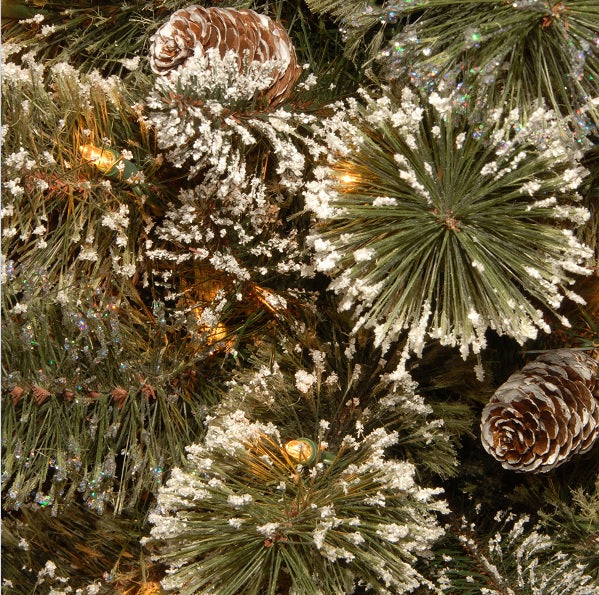 Pre-lit tree in a pot. The branches are covered in white glitter and there are pine cone accents. The lights are clear.