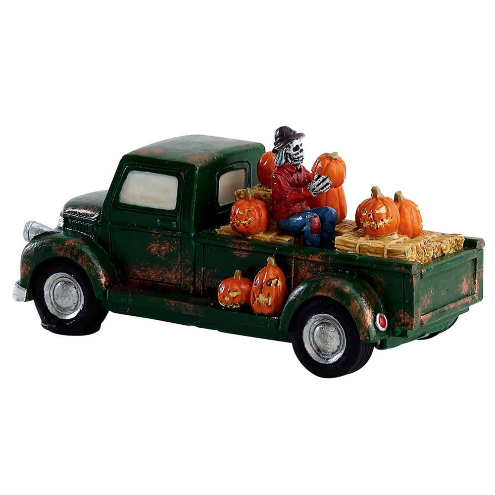 Polyresin figure for a Lemax display. Designed to look like rusty, old green pickup truck carrying a bunch of jack-o-lanterns, bales of hay and a skeleton wearing a red shirt and jeans.
