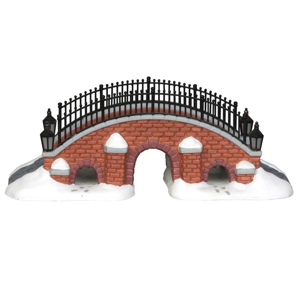 Porcelain lighted building for a Lemax display. Designed to look like a brick bridge with a metal fence. The path on the bridge is made of stone. There's snow on the ground and you can see footsteps in the snow.