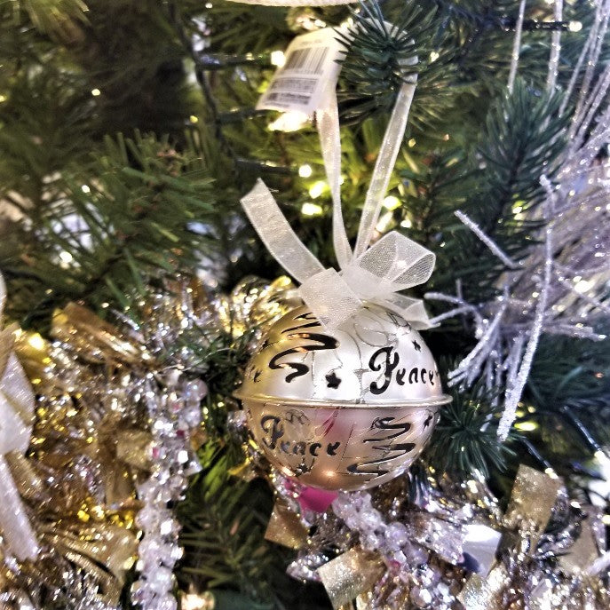 Gold bell ornament. There are swirl cutouts and a cutout that reads "PEACE."