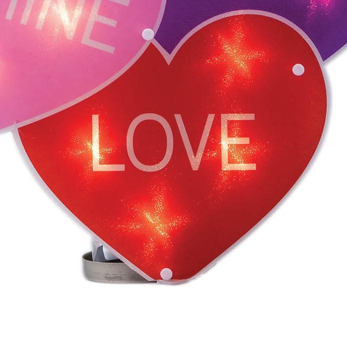 A light up decoration for Valentine's Day designed to look like three conversation hearts. One is purple and reads "XOXO." One is pink and reads "BE MINE." The other is red and reads "LOVE."