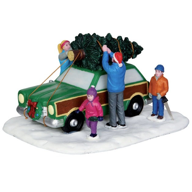 Polyresin figurine for a Lemax Village tabletop display. Designed to look like a family of four tying a Christmas tree to the top of their green and brown Vista Cruiser car. There's a small wreath with a red ribbon on the front bumper of the car. The ground is covered in snow. The young boy is holding a saw and the dad is wearing a Santa hat.