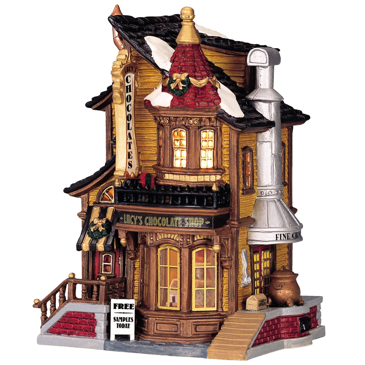Porcelain lighted building for a Lemax display. Designed to look like an old Victorian-era house with wreaths and snow on it. The house is gold with brown frames. Inside the window you can see an array of chocolates.