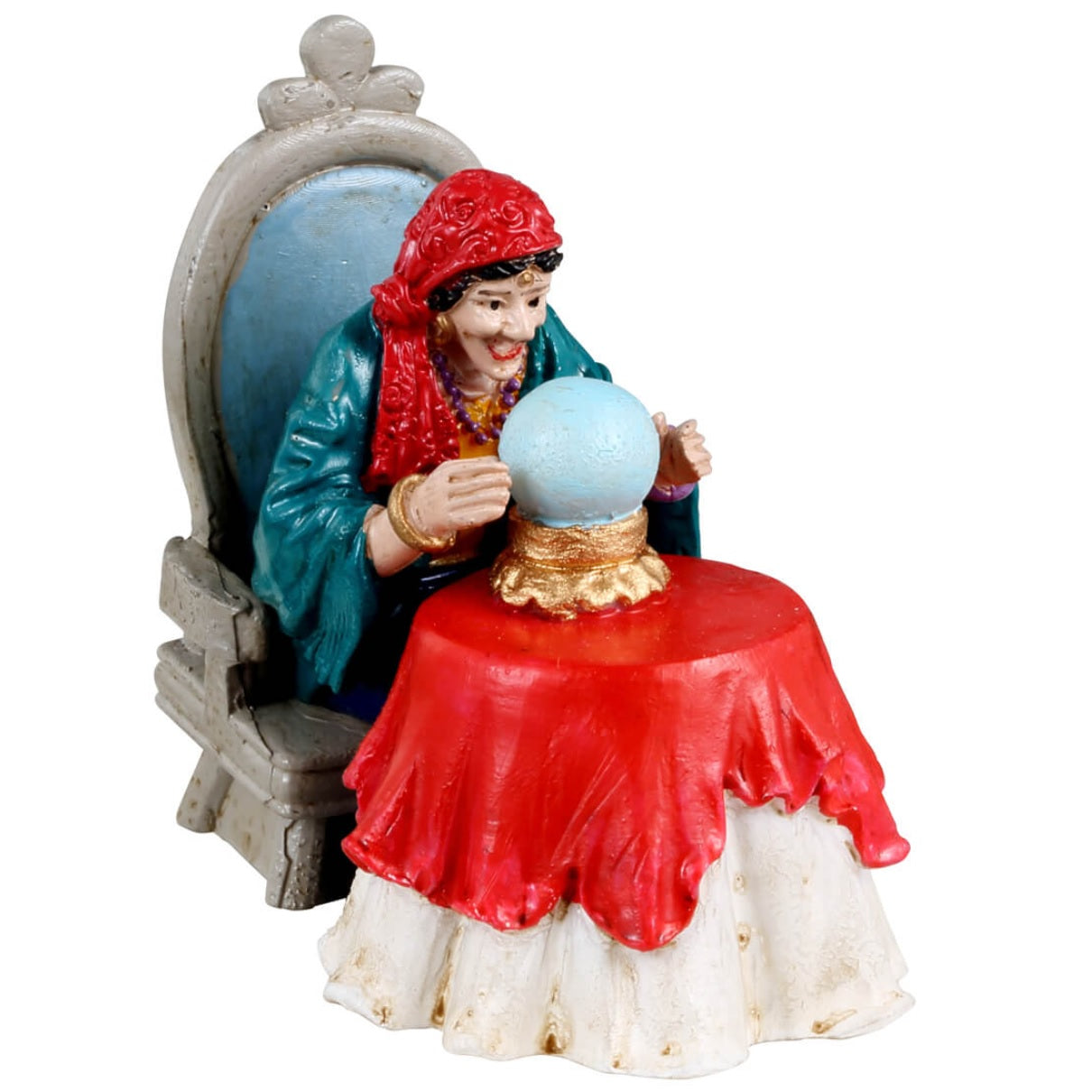 Resin figurine for a Lemax Spooky Town display. Designed to look like a psychic reading from her crystal ball. She's sitting in a gray chair with blue cushion. She's wearing a red head scarf and a blue shawl. The table has a white tablecloth on it with a red tablecloth over it. The crystal ball is on a gold stand.
