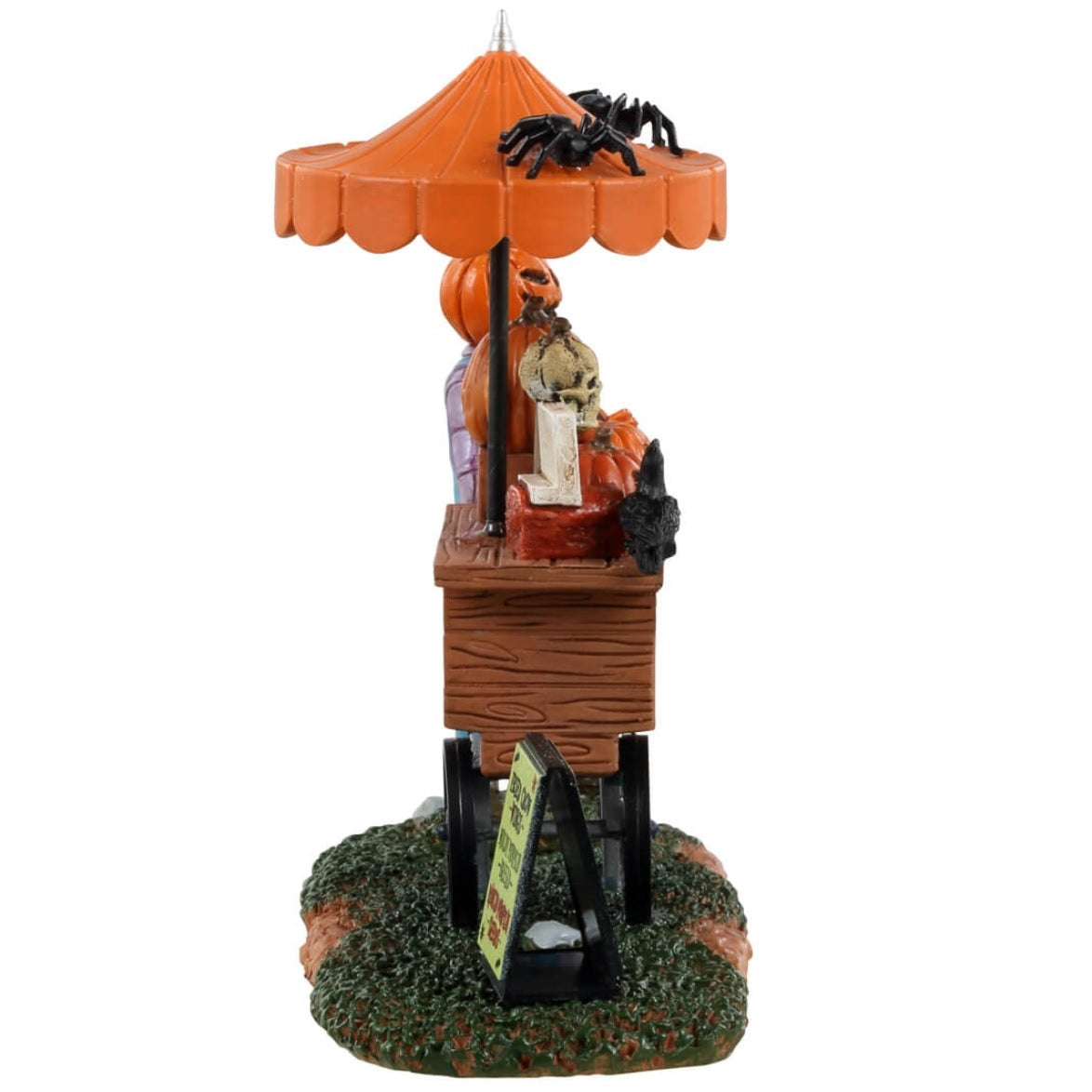 Resin table accent for a Lemax display. Designed to look like a scarecrow with a pumpkin head standing in front of a cart full of carved pumpkins. There's an orange umbrella above the cart with spiders on top. There's a sign on the ground that reads "Fried crow wings, moldy pumpkin bread and rancid pumpkin seeds."