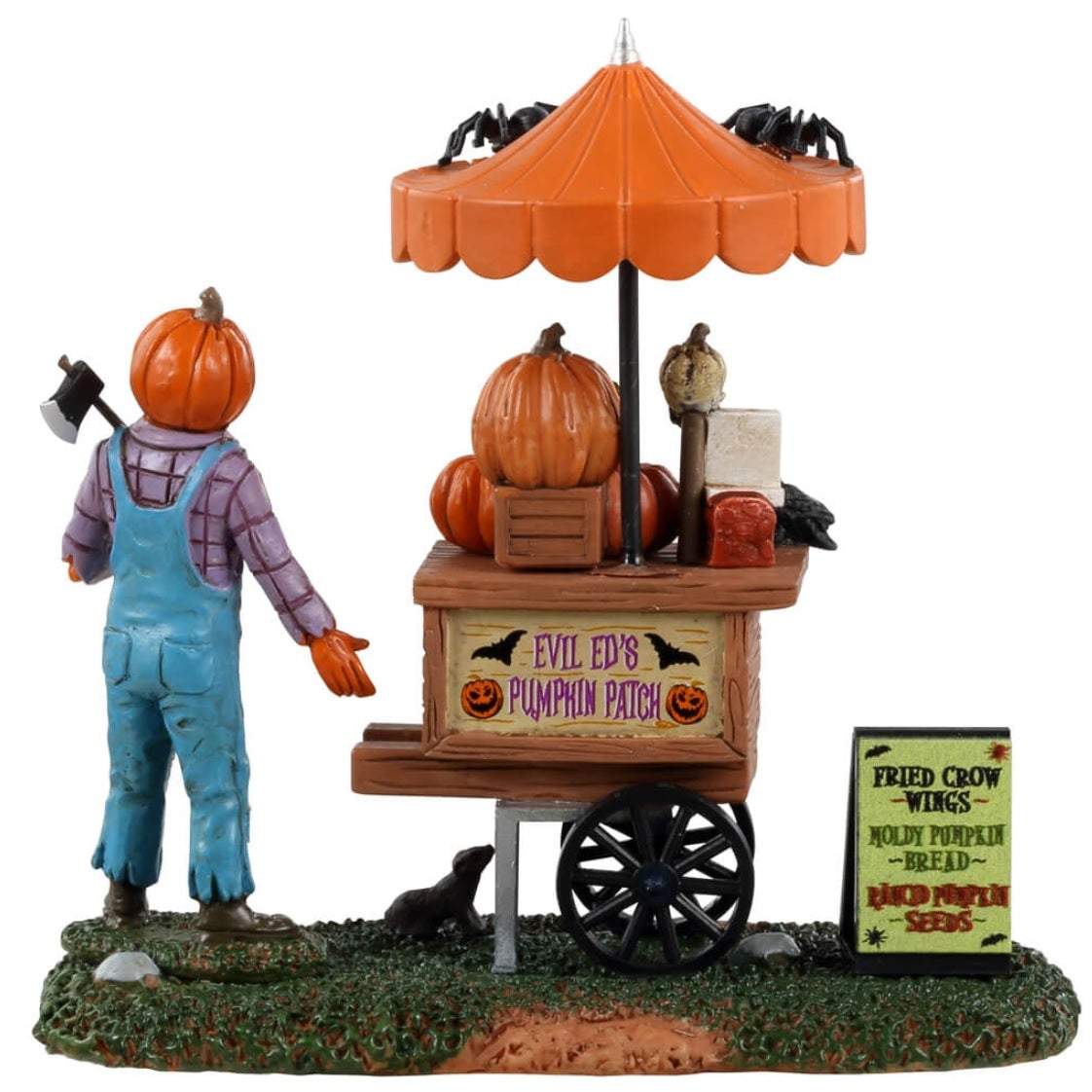 Resin table accent for a Lemax display. Designed to look like a scarecrow with a pumpkin head standing in front of a cart full of carved pumpkins. There's an orange umbrella above the cart with spiders on top. There's a sign on the ground that reads "Fried crow wings, moldy pumpkin bread and rancid pumpkin seeds."