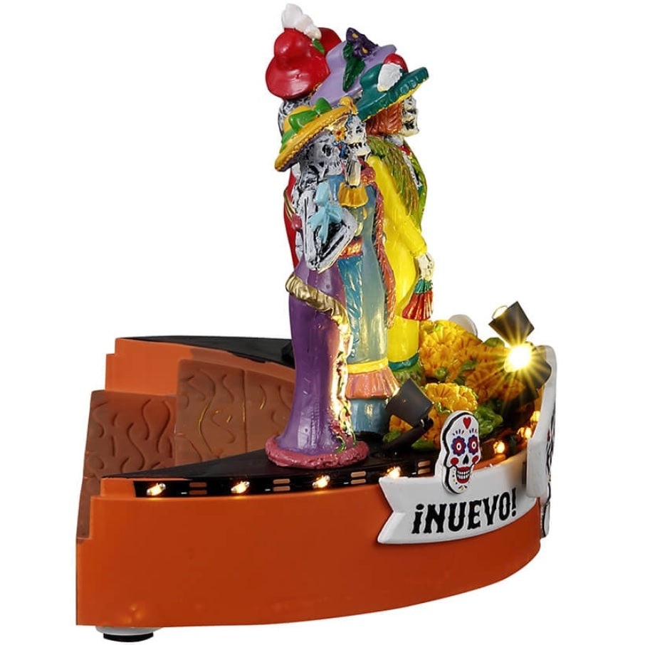 Resin accent for a Lemax Spooky Town display. Designed to look like five skeletons dressed in gaudy, brightly colored costumes. There are signs that read "Nuevo," "Dia de los Muertos Fashion Show" and "Elegante!" Designed to look like they're on stage at a fashion show. There are sugar skull accents and flowers on the stage.