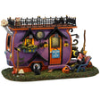 Resin village accent for a Lemax display. Designed to look like a purple, orange and black camper van parked on a patch of grass. There are mushrooms and carved pumpkins and black cats and an owl. There's a witch sitting in a blue chair.