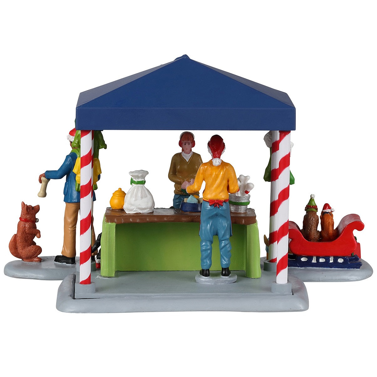 Resin table accent for a Lemax display. Designed to look like a booth that sells pet treats. It's decorated for Christmas. There's a woman handing her dog a bone while another is purchasing some food for her dog who is wearing red booties. There are two dogs wearing Santa hats in a red sleigh posing for pictures.
