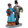 Resin figurine for a Lemax display. Designed to look like a man and a woman walking arm in arm. They're both wearing older Victorian-era type clothes and holding presents.