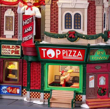 Resin lighted building for a Lemax display. Designed to look like a pizza shop. It's decorated for Christmas and there's snow on the sidewalk. Inside the window, you can see a chef spinning dough in the air. There's a circular pizza sign on the roof.