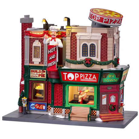Resin lighted building for a Lemax display. Designed to look like a pizza shop. It's decorated for Christmas and there's snow on the sidewalk. Inside the window, you can see a chef spinning dough in the air. There's a circular pizza sign on the roof.