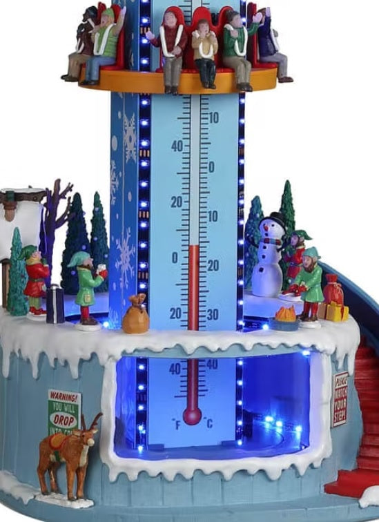 Resin village accent for a Lemax display. Designed to look like a winter-themed carnival ride. Santa and a reindeer stand on the top. There are people on the ride and people standing in line. The backdrop of the ride is designed to look like a thermometer.