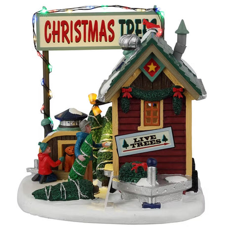 Resin lighted building for a Lemax display. Designed to look like a small shack. There are solar panels and snow on the roof. The door is open and there's a person inside selling Christmas trees and wreaths. There's a young child and a dog checking out some of the trees off to the side.
