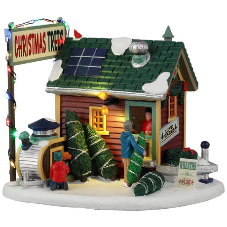 Resin lighted building for a Lemax display. Designed to look like a small shack. There are solar panels and snow on the roof. The door is open and there's a person inside selling Christmas trees and wreaths. There's a young child and a dog checking out some of the trees off to the side.