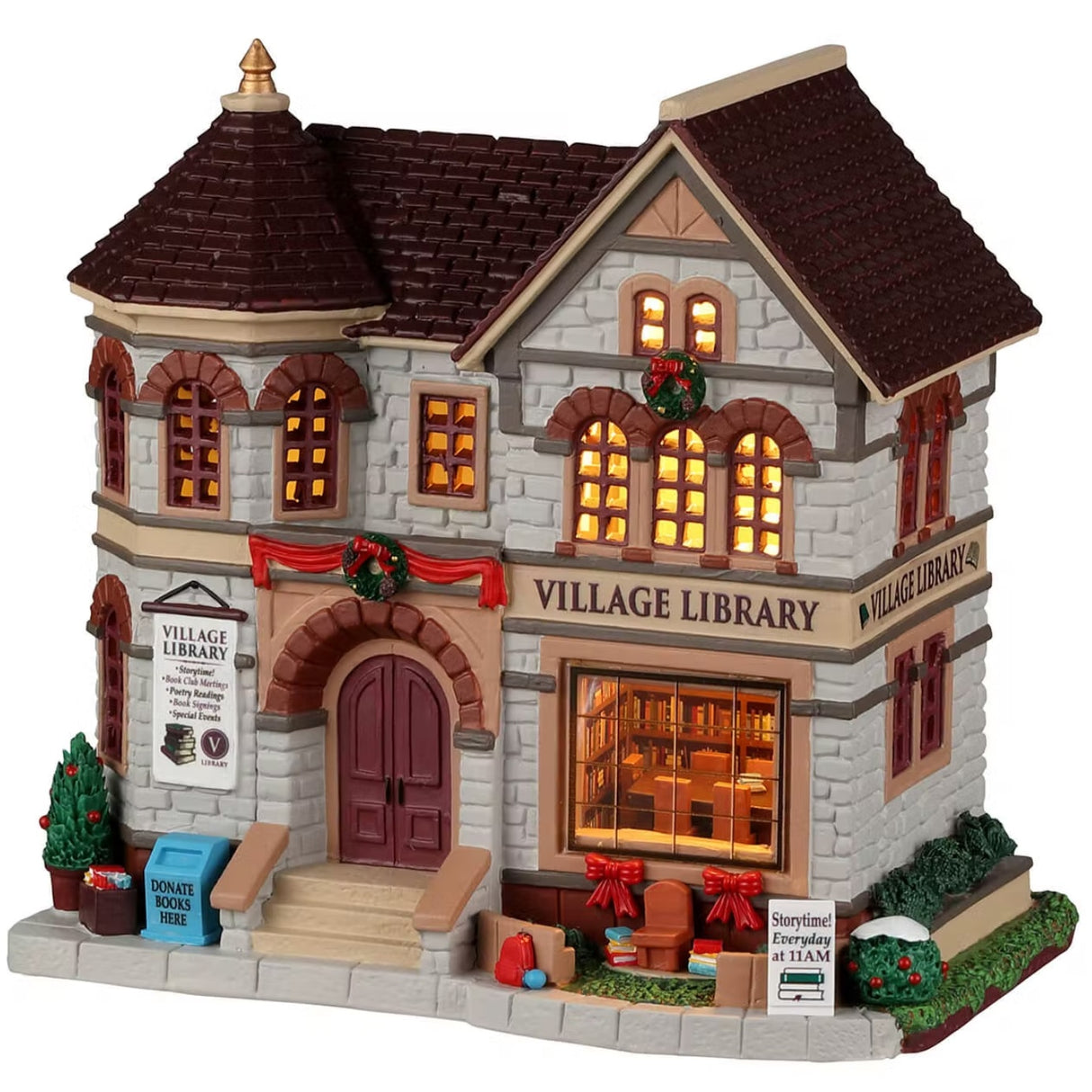Porcelain lighted building for a Lemax display. Designed to look like a gray brick village library. There are red ribbon accents and decorated wreaths. Inside the window, you can see shelves of books and a table with chairs. There's a sign that reads "STORY TIME EVERY DAY AT 11 AM." There's a little snow on some of the bushes on the side.