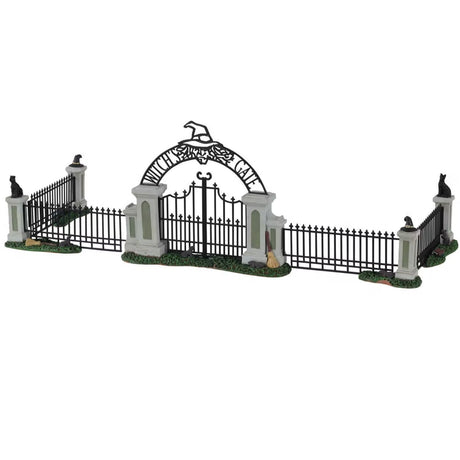 Polyresin village accessory for a Lemax display. Designed to look like an iron fence on patches of grass. There are four columns with witch hat and black cat statues on top. The gate reads "Witch's Gate" and there's a broom leaning against it.