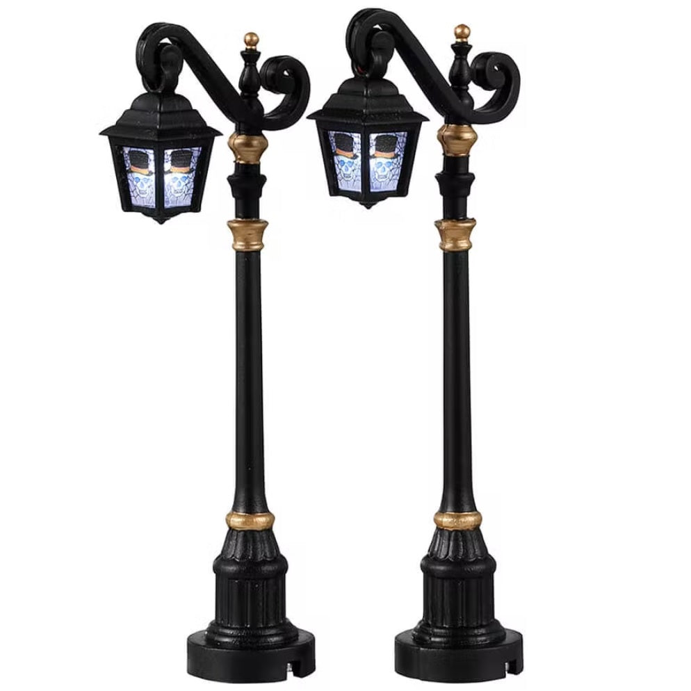Plastic village accessories for a Lemax display. Designed to look like regal lampposts. They're shiny black with gold accents. The glass on the light has a skeleton wearing a black top hat.