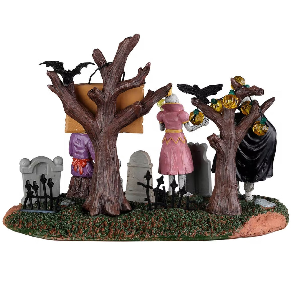 Resin village accent for a Lemax Spooky Town display. Designed to look like three skeletons wearing costumes in a graveyard. One skeleton is dressed like a vampire, one skeleton is dressed like a princess and the other skeleton is dressed like a witch and is petting a skeleton dog. The trees are decorated with pumpkin lights and there are black crows sitting on some branches.