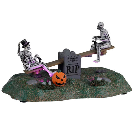 Resin village accent for a Spooky Town Lemax display. Designed to look like two skeletons on a teeter totter. One skeleton is wearing a top hat and has his leg on a carved pumpkin. There are two gravestones in the middle of the teeter totter that read RIP.