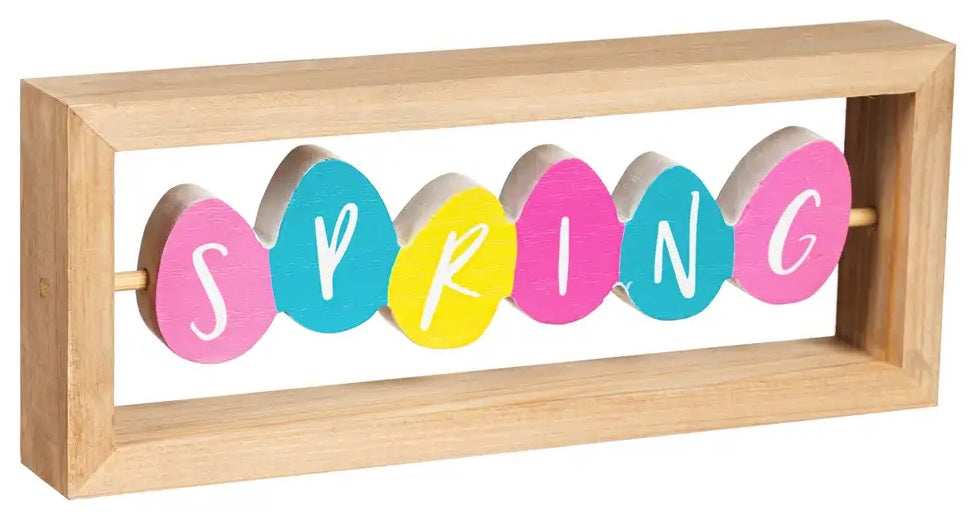 A rectangular wooden tabletop decoration made up of brightly colored eggs. The side that is shown here reads SPRING. The eggs are pink, light blue, yellow and bright pink