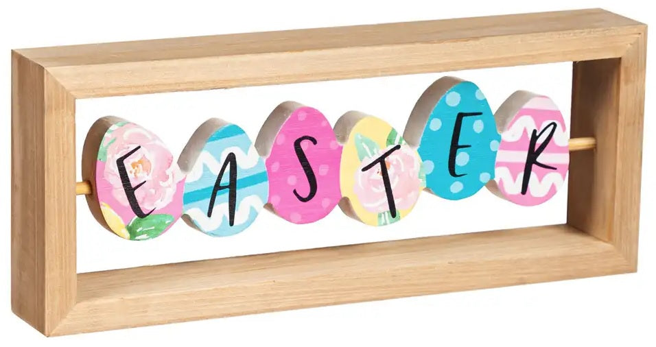 A rectangular wooden tabletop decoration made up of brightly colored eggs. The side that is shown here reads EASTER. Each egg has a different pattern on it. The colors are pink, light blue, green, pink, white, teal and yellow