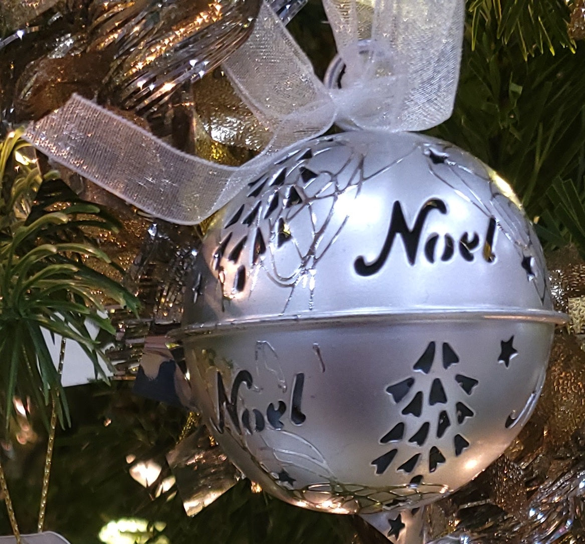 Silver bell ornament with tree and star cutouts and cutouts that read "NOEL."