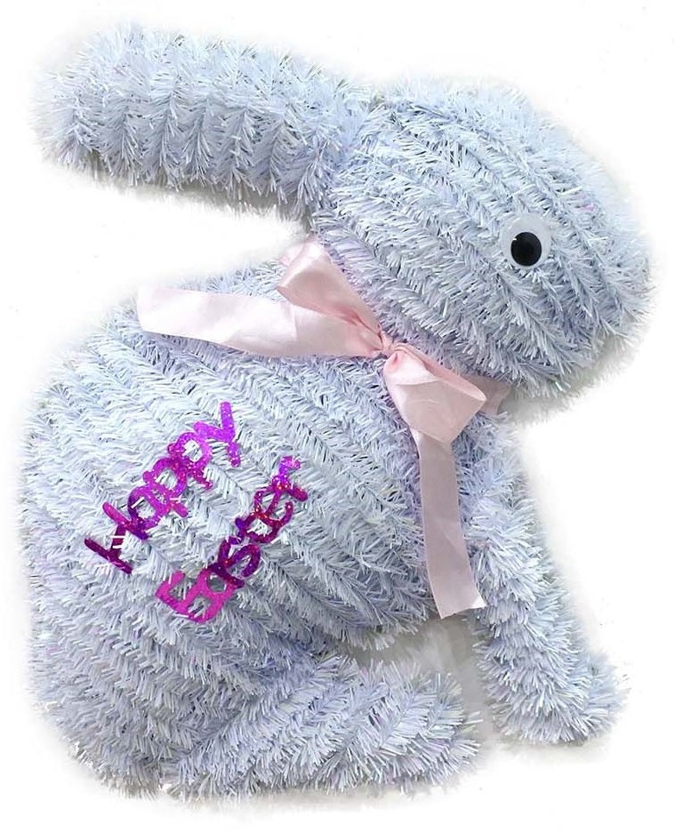 A white tinsel tabletop decoration shaped like bunnies that read "HAPPY EASTER" and features a light pink bow around its neck