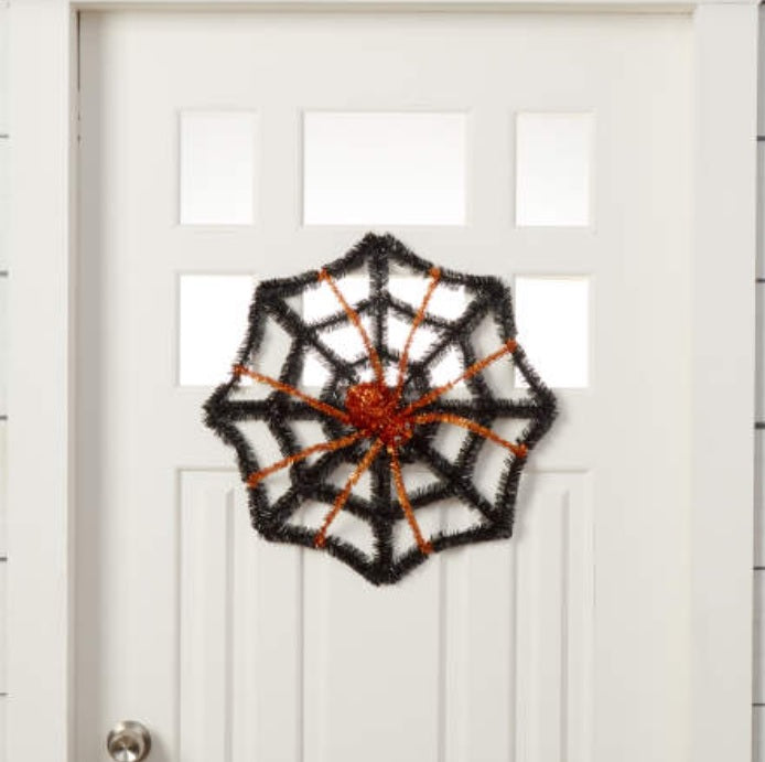 Black tinsel decoration shaped like a web with a spider in the center. One features a purple spider and the other features an orange spider.