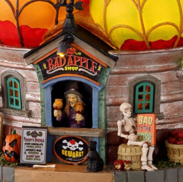 Polyresin building for a Lemax display. Designed to look like a building with a roof made out of giant apples. There's a witch at the front booth handing out caramel covered apples. There are snakes, owls, black cats, tombstones, a skeleton sitting on a barrel and a barrel of apples.
