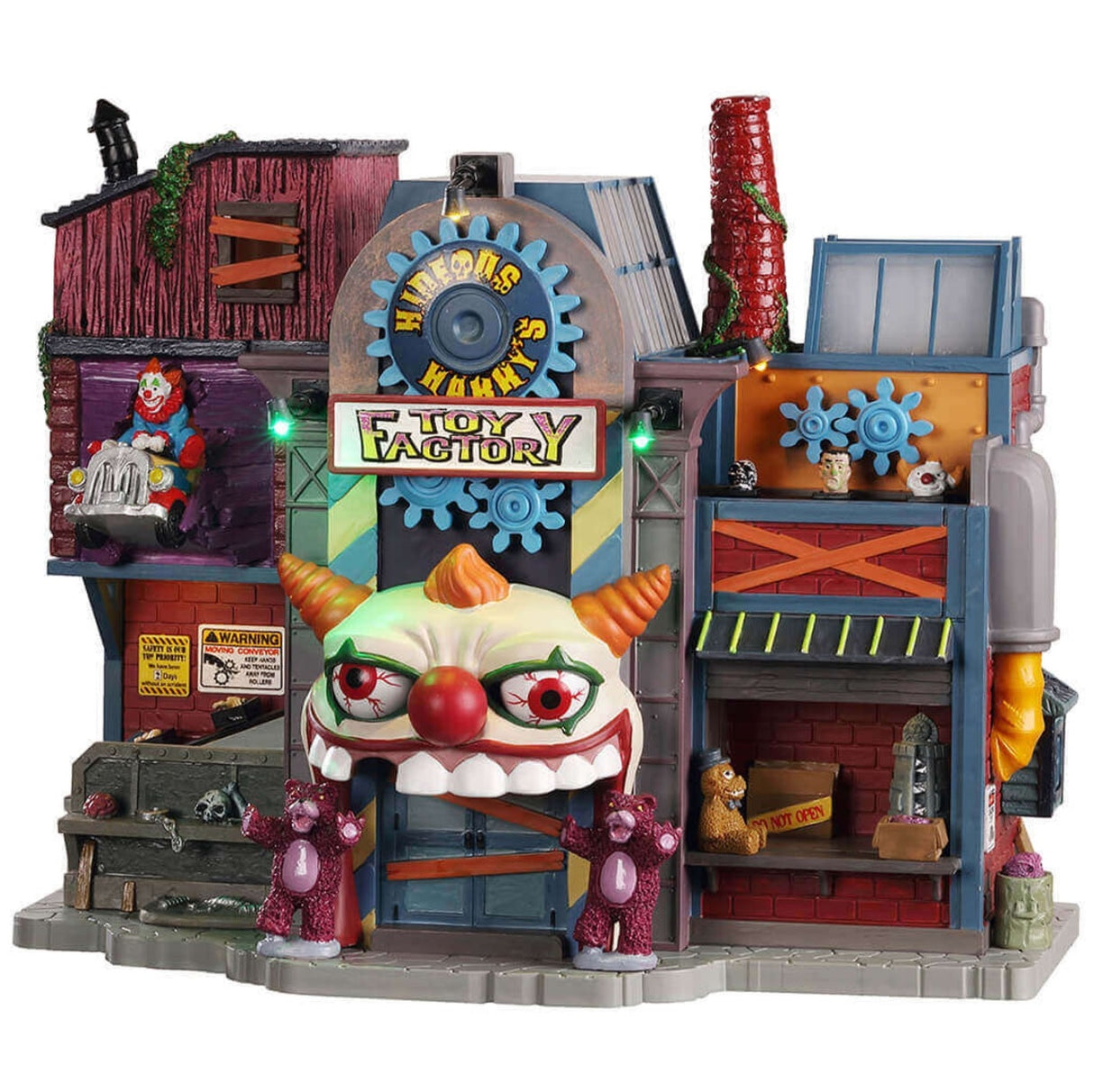 Plastic building for a Lemax display. Designed to look like a a very unique toy factory. The roof over the front door is shaped like a clown's face and mouth. There are two purple teddy bears standing next to the front door. There are gears, teddy bears, skulls and vines everywhere. The windows are boarded up.