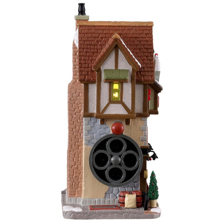 Porcelain lighted building for a Lemax display. Designed to look like a tall cottage. The sign reads "The Coffee Bean Grinder. Quality beans." You can see shelves of cups in the front window. There's snow on the building and features a few small trees in pots shaped like mugs. There's a crank on the side of the building for decoration.