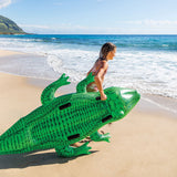 This is a lifestyle image showing a young girl dragging this crocodile inflatable on the beach toward the water.
