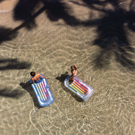 This is a lifestyle image showing two people bringing their inflatable chairs out of the ocean onto the beach.