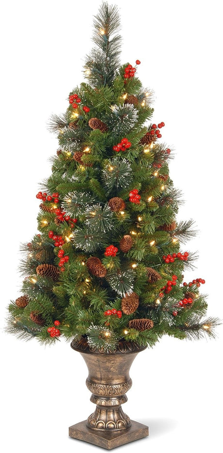 Artificial tree in a bronze pot pre-lit with clear lights. Some of the branches have white glitter on them. There are pine cones and berry accents.