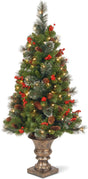 Artificial tree in a bronze pot pre-lit with clear lights. Some of the branches have white glitter on them. There are pine cones and berry accents.