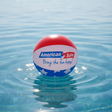 This is a lifestyle image showing a beach ball on top of the water. The beach ball is red, white and blue striped and reads "American Sale. Bring the fun home!"