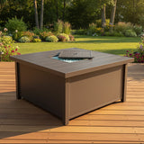 This is a lifestyle image showing what this fire pit table looks like on a wooden patio in a grassy backyard on a sunny day.