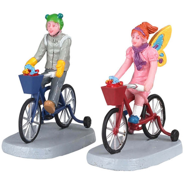 Polyresin figurines for a Lemax display. Designed to look like two children dressed up for Halloween. The boy is dressed like an alien and riding a blue tricycle. The girl is dressed like a butterfly and riding a red tricycle. They both have baskets full of candy on their bikes.