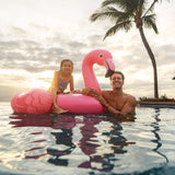 This is a lifestyle image showing a young girl sitting on this flamingo float in a pool while her dad holds the head of the float.