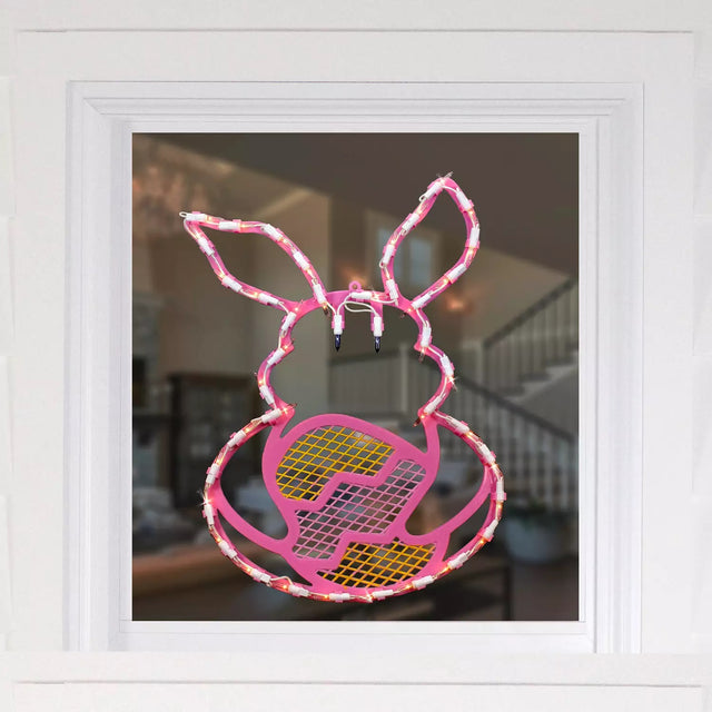 A mock up of what this pink window silhouette would look like against a window. The decoration is shaped like a bunny holding an egg