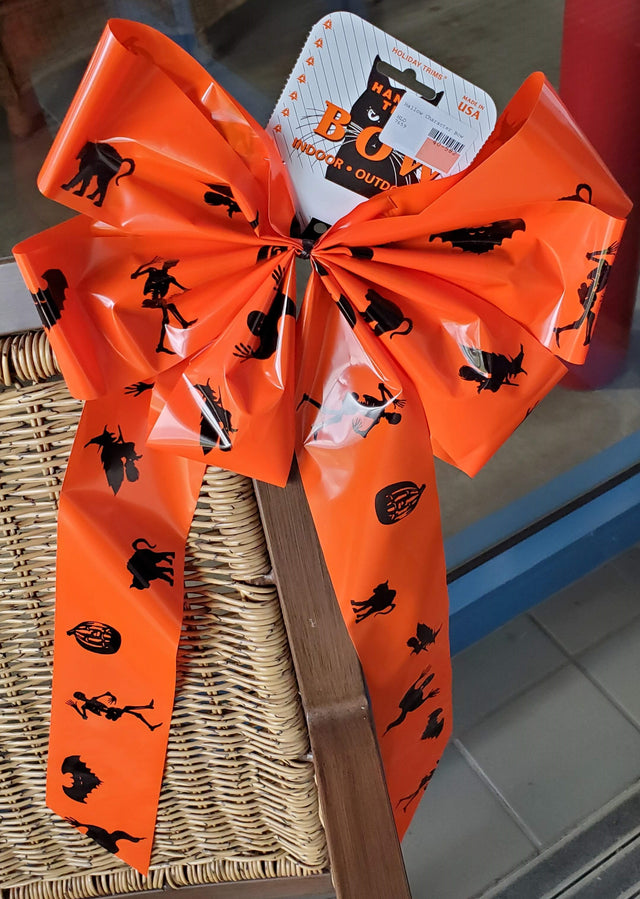 Orange bow with black figures on it. The figures include a skeleton, a pumpkin, a cat, a switch on a broom and a bat.