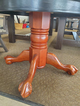 Round, wooden table. Tabletop is black and the legs are a cherry wood color.