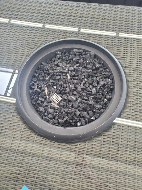 Square fire pit table. Made of woven materials. Features a lid. Underneath the lid is fire glass.