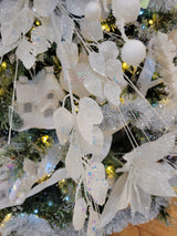 This is a lifestyle image showing the white iridescent pick spray in a tree surrounded by other garland, ornaments and lights.