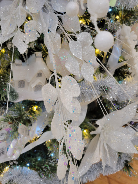 This is a lifestyle image showing the white iridescent pick spray in a tree surrounded by other garland, ornaments and lights.