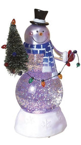 Glass snowman decoration. The snowman is wearing a black top hat, a blue and white scarf and red gloves. He's holding a small tree with a string of multi-colored lights. There's glitter inside.