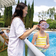 This is a lifestyle image showing a mom adjusting the strap on the goggles that a young girl is wearing inside the pool.