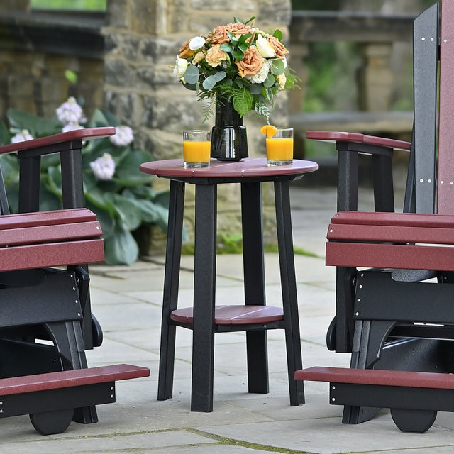 This is a lifestyle image showing the Cherrywood and Black colored end table between two matching Adirondack chairs. On top of the table is a vase of flowers and two cups of orange juice.