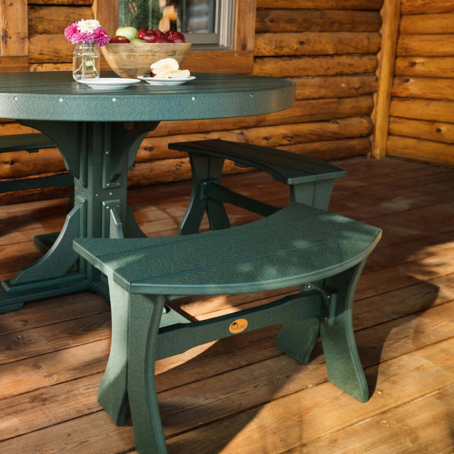 This is a lifestyle image showing the Green colored Table Bench around a matching table on a wooden deck in front of a log cabin-style house.
